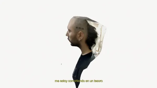 In a white background, there's an image cut and pasted of a person seeing from the side, wearing a black T-shirt. Hair and barb are shaved, but the black hair at the back is longer, and one can see an earring in the left ear. Below, in yellow, are the words me estoy conviertiendo en un tesoro (I am becoming a treasure).
